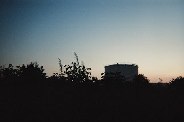 Distant building silhouette at dusk above a dark treeline with a gradient sunset horizon