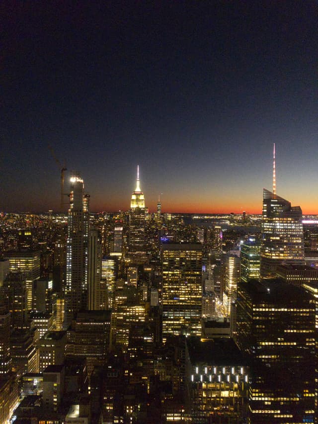 A city skyline at dusk with illuminated skyscrapers and a darkening sky