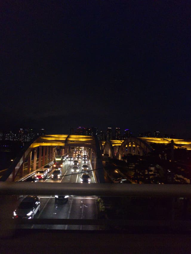 A nighttime view of a bridge with illuminated arches and vehicles traveling on it, set against a dark sky