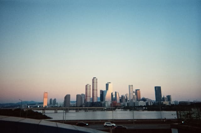 Seoul city skyline across the Han River at dusk, with high-rise towers silhouetted against a pastel sunset
