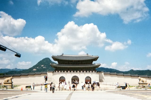 Visitors at Gwanghwamun Gate of Gyeongbokgung Palace under a blue sky with clouds