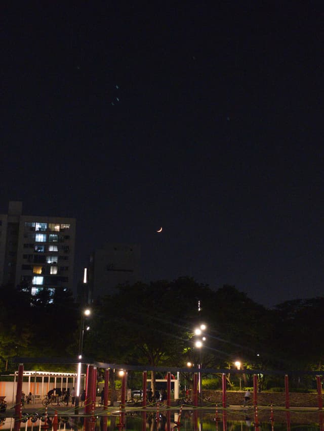 A nighttime scene with a crescent moon in the sky, city lights, and a building in the background