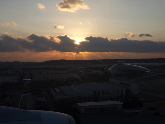 A sunset over an airport with clouds partially obscuring the sun, casting a warm glow across the sky