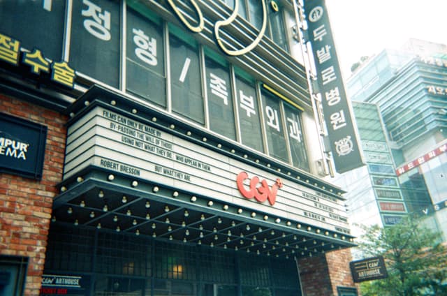 Movie theater entrance with illuminated marquee and vertical Korean signage in a city street
