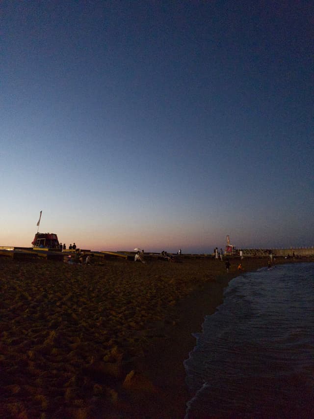 A beach during twilight with vehicles parked along the shore and gentle waves lapping against the sand