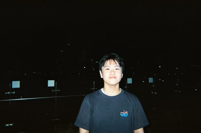 Person standing outdoors at night against a dark cityscape background