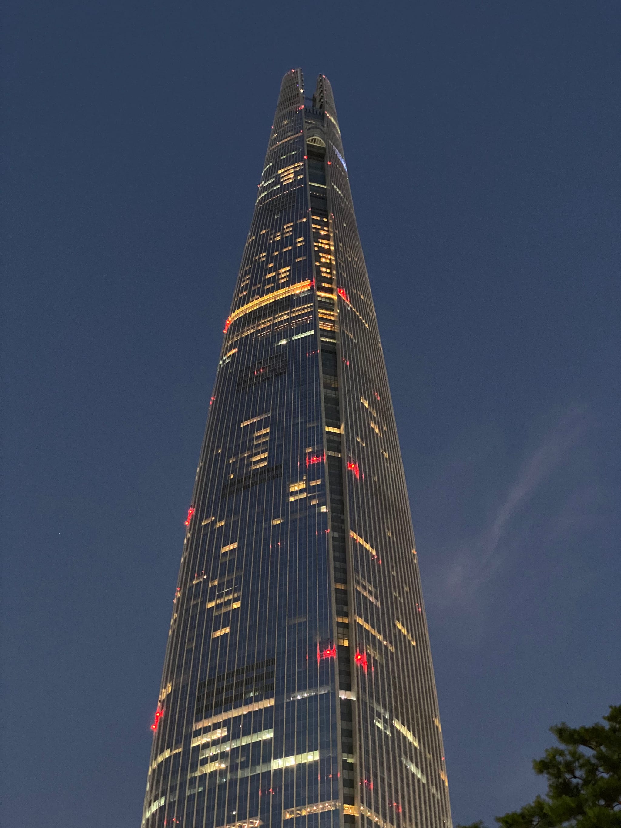 A tall, illuminated skyscraper with a sleek, tapering design against a dark evening sky