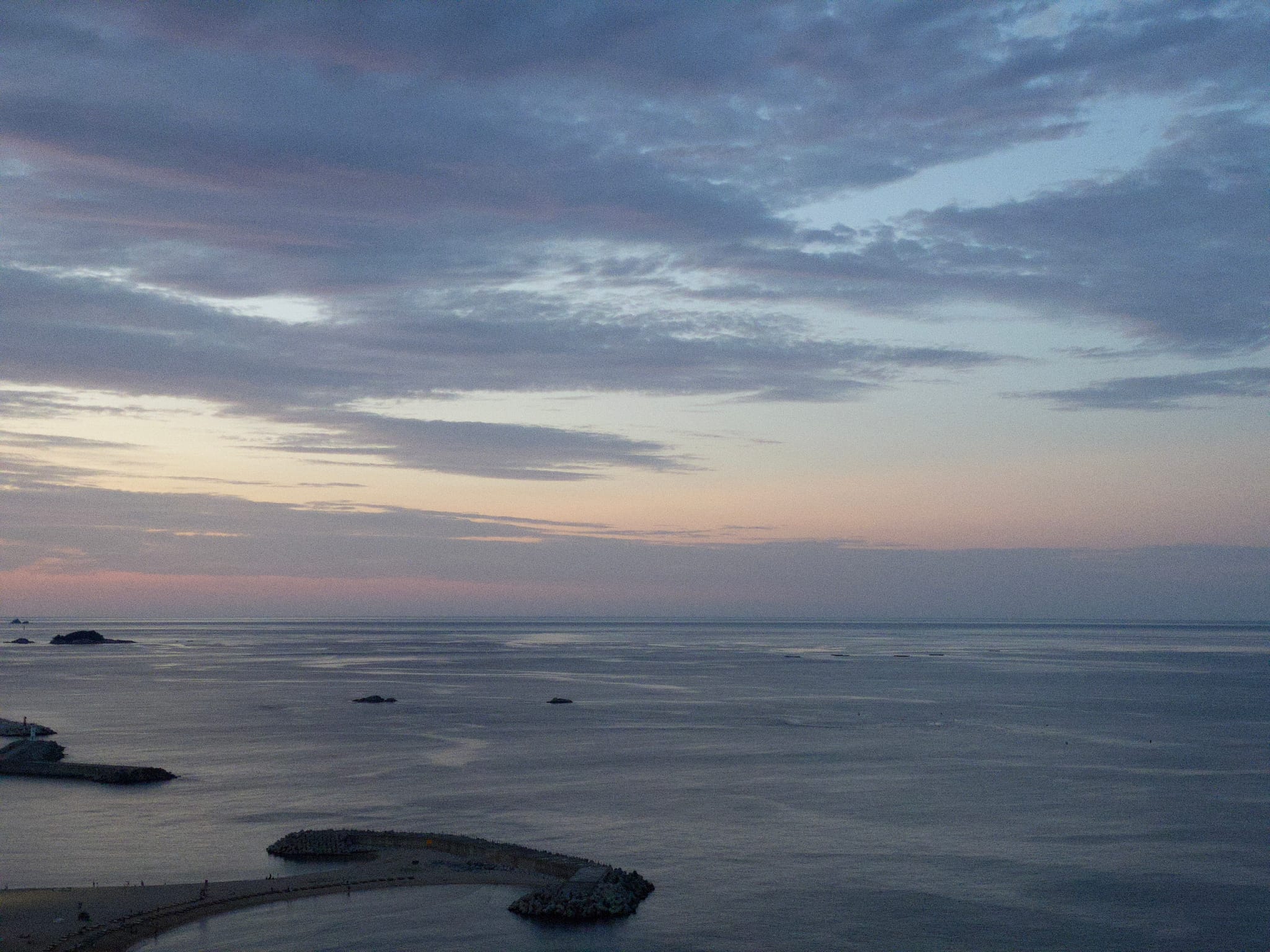 A serene coastal view at dusk with calm waters, scattered clouds, and small rocky formations