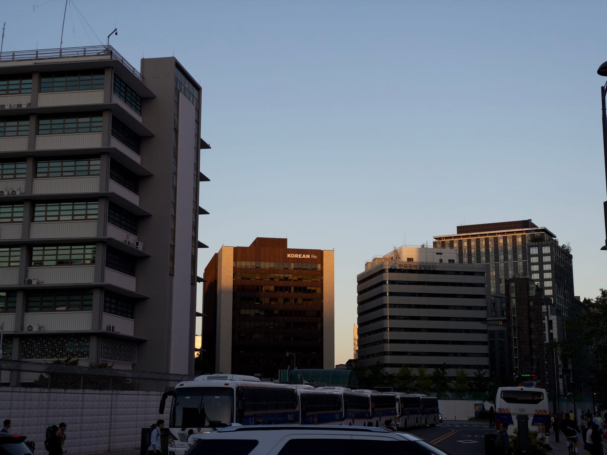 High-rise buildings silhouetted against a clear evening sky with vehicles in the foreground