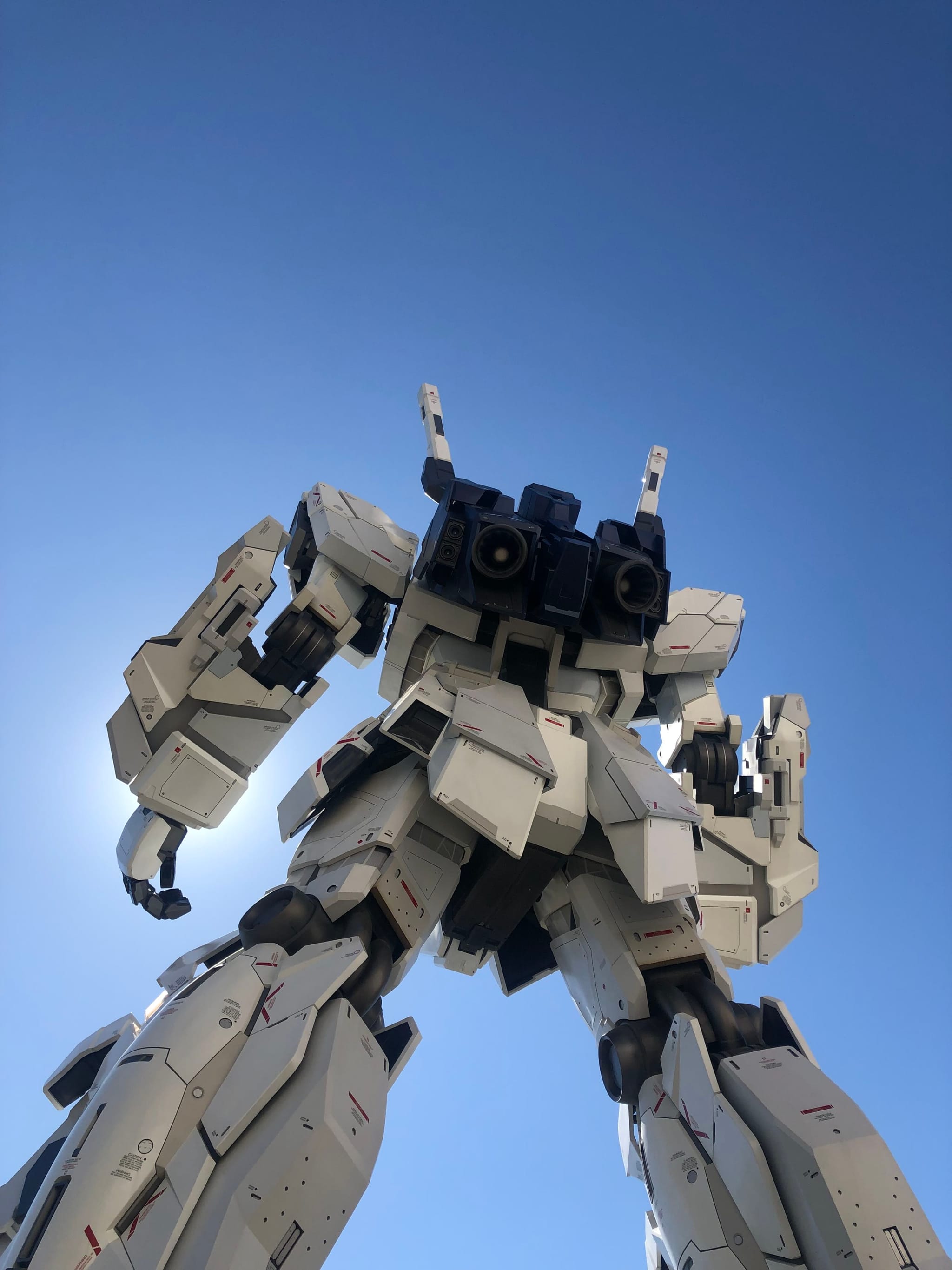 A large, white robot statue viewed from below against a clear blue sky