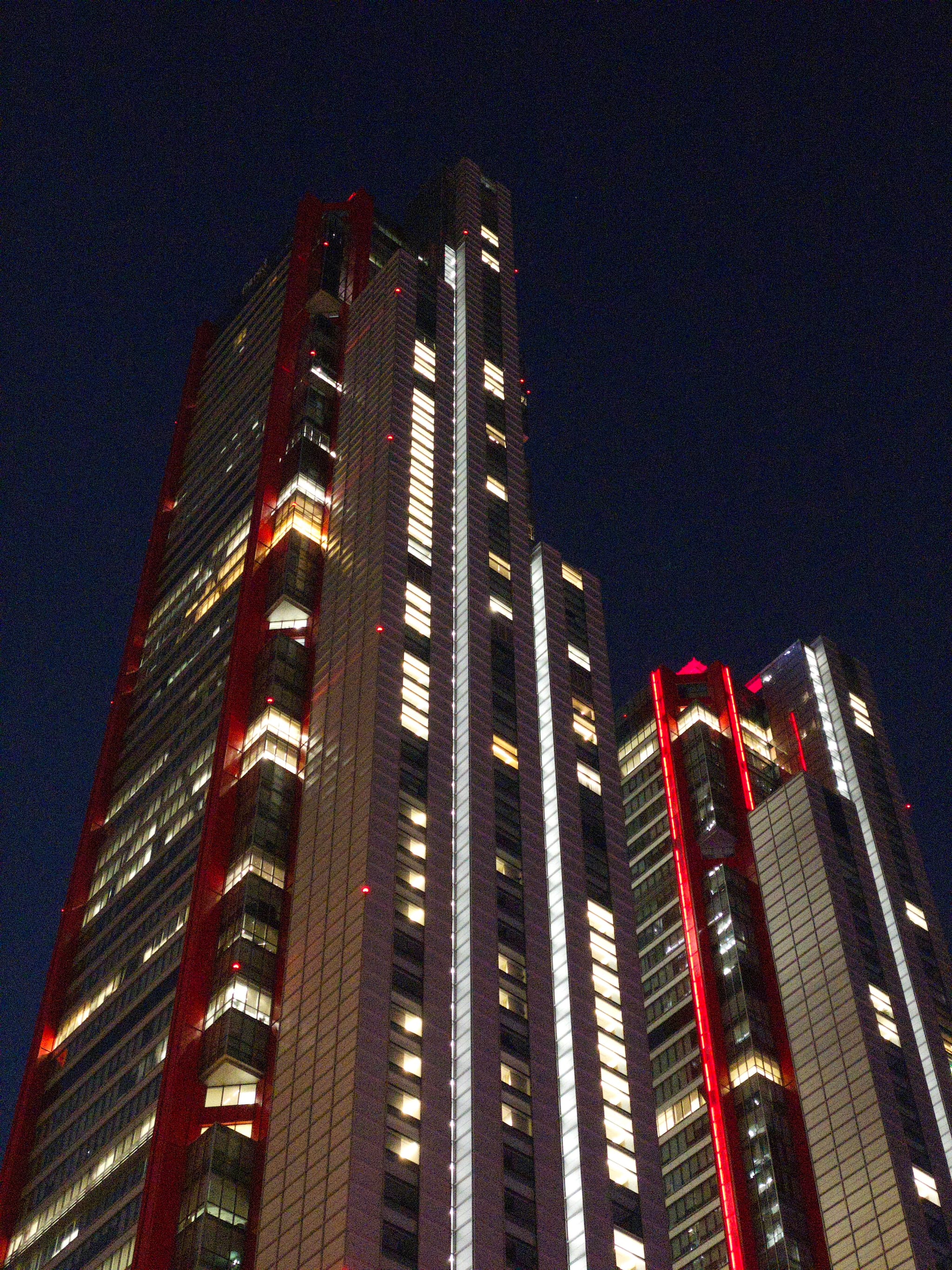 Tall skyscrapers with illuminated windows and red accents against a dark night sky
