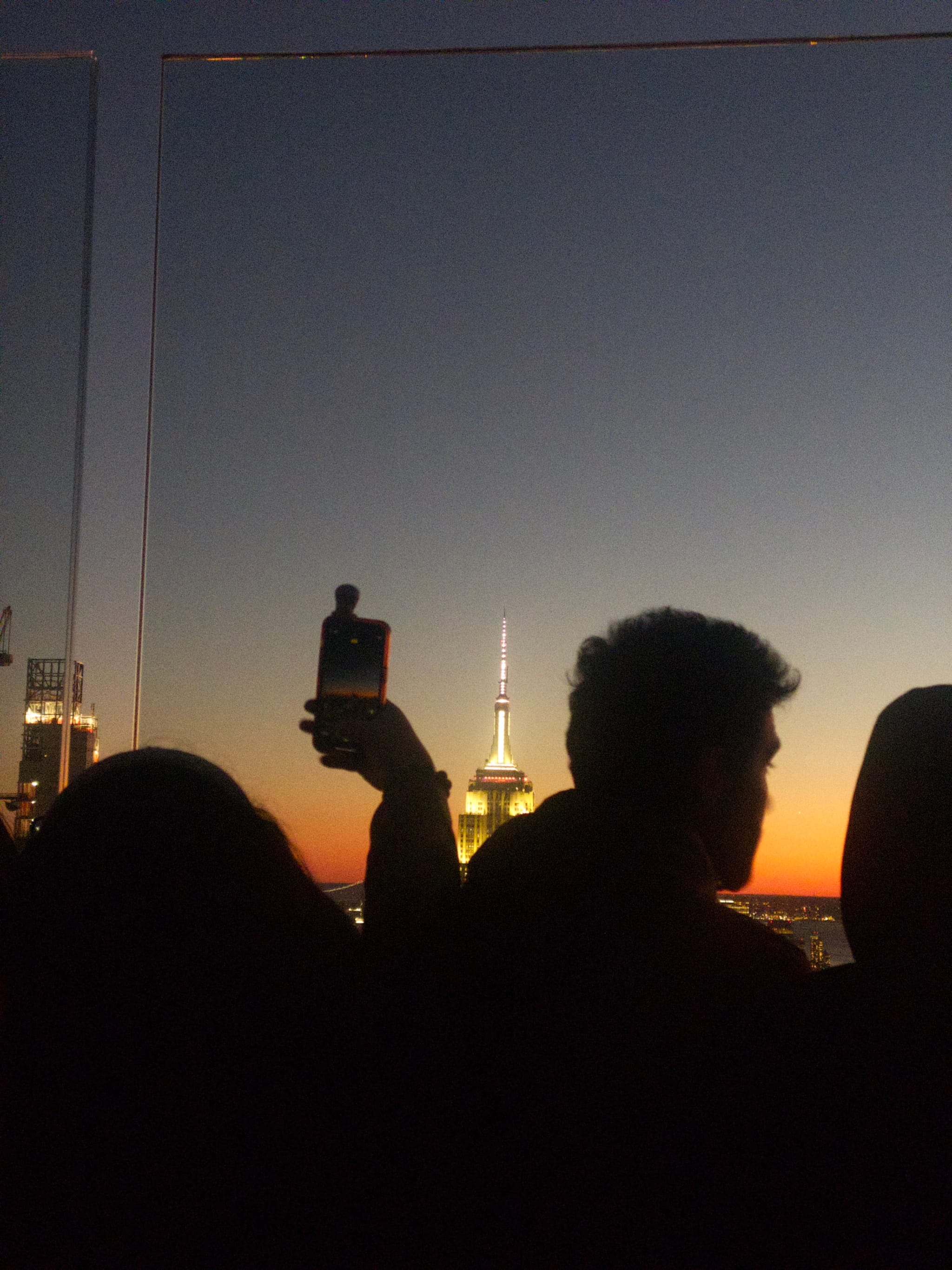 Silhouetted people against a sunset skyline, with one person holding up a bottle, and a prominent tower in the background