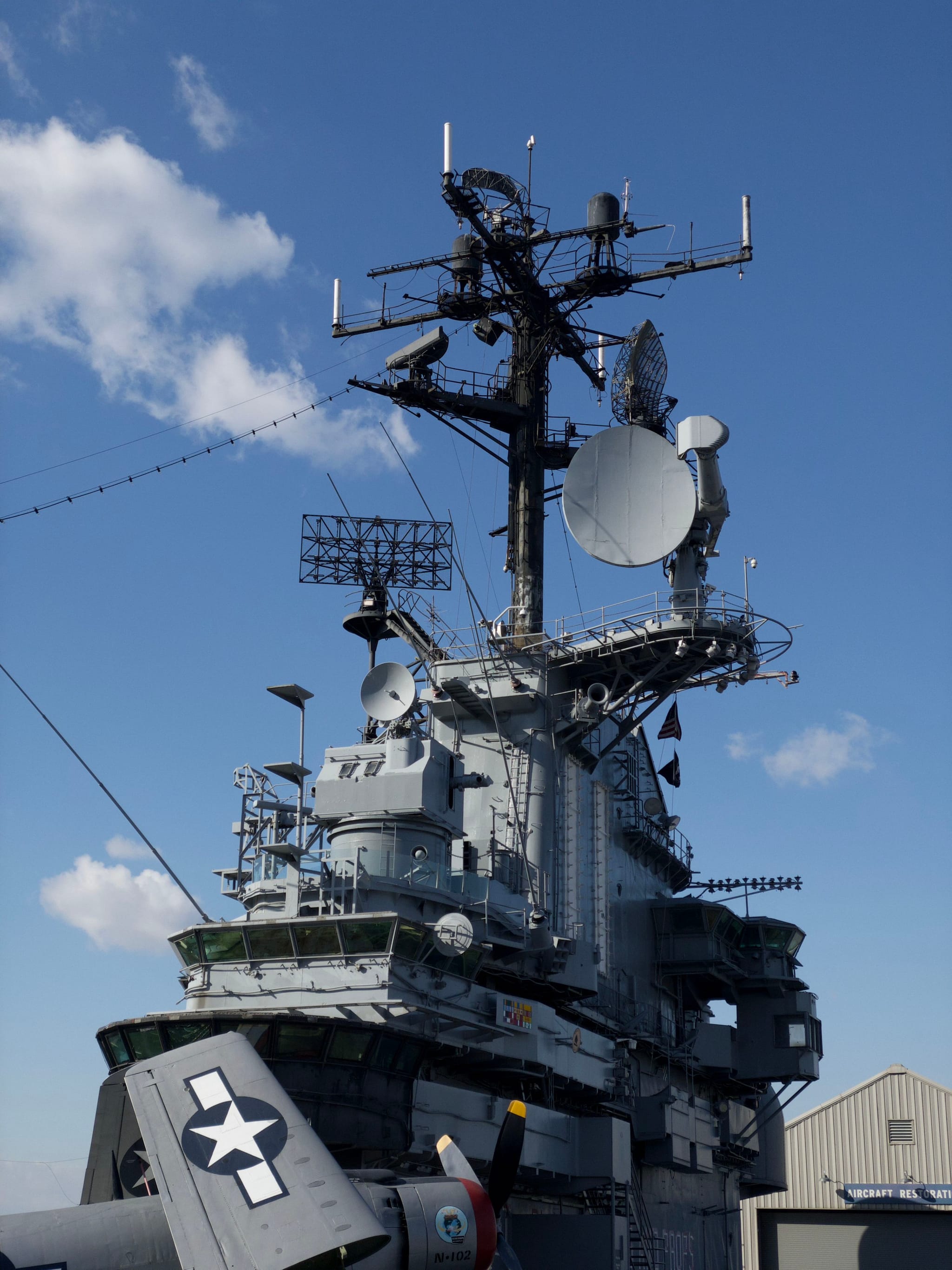 A naval ship's communication and radar tower with various antennas and equipment against a clear blue sky