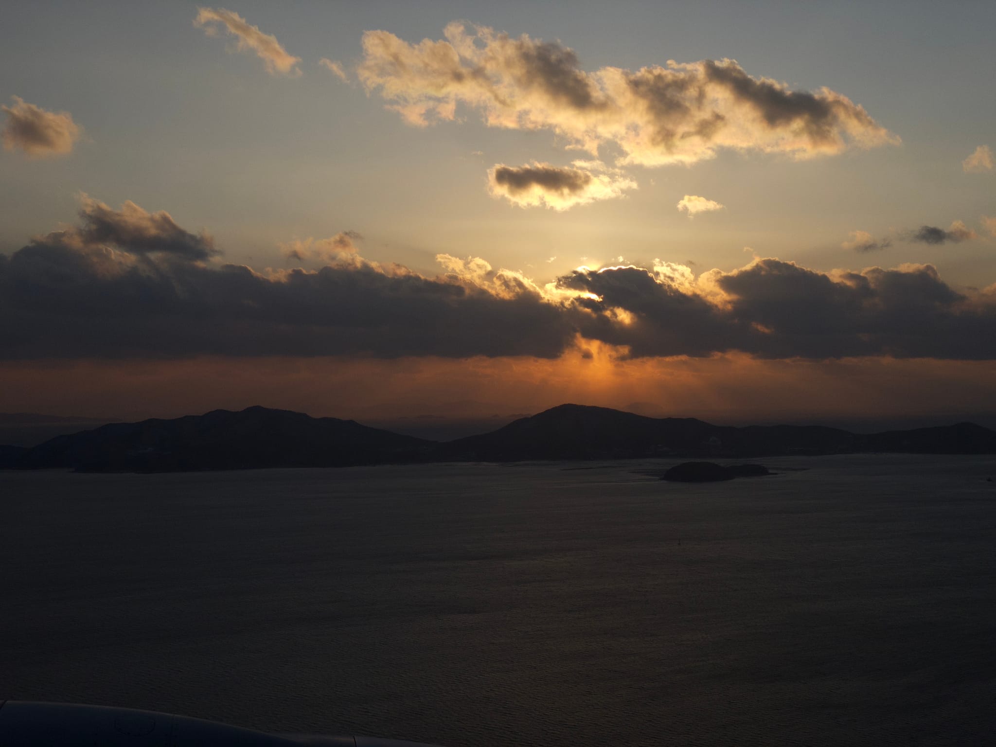 A sunset over a body of water with silhouetted hills and clouds, creating a dramatic sky