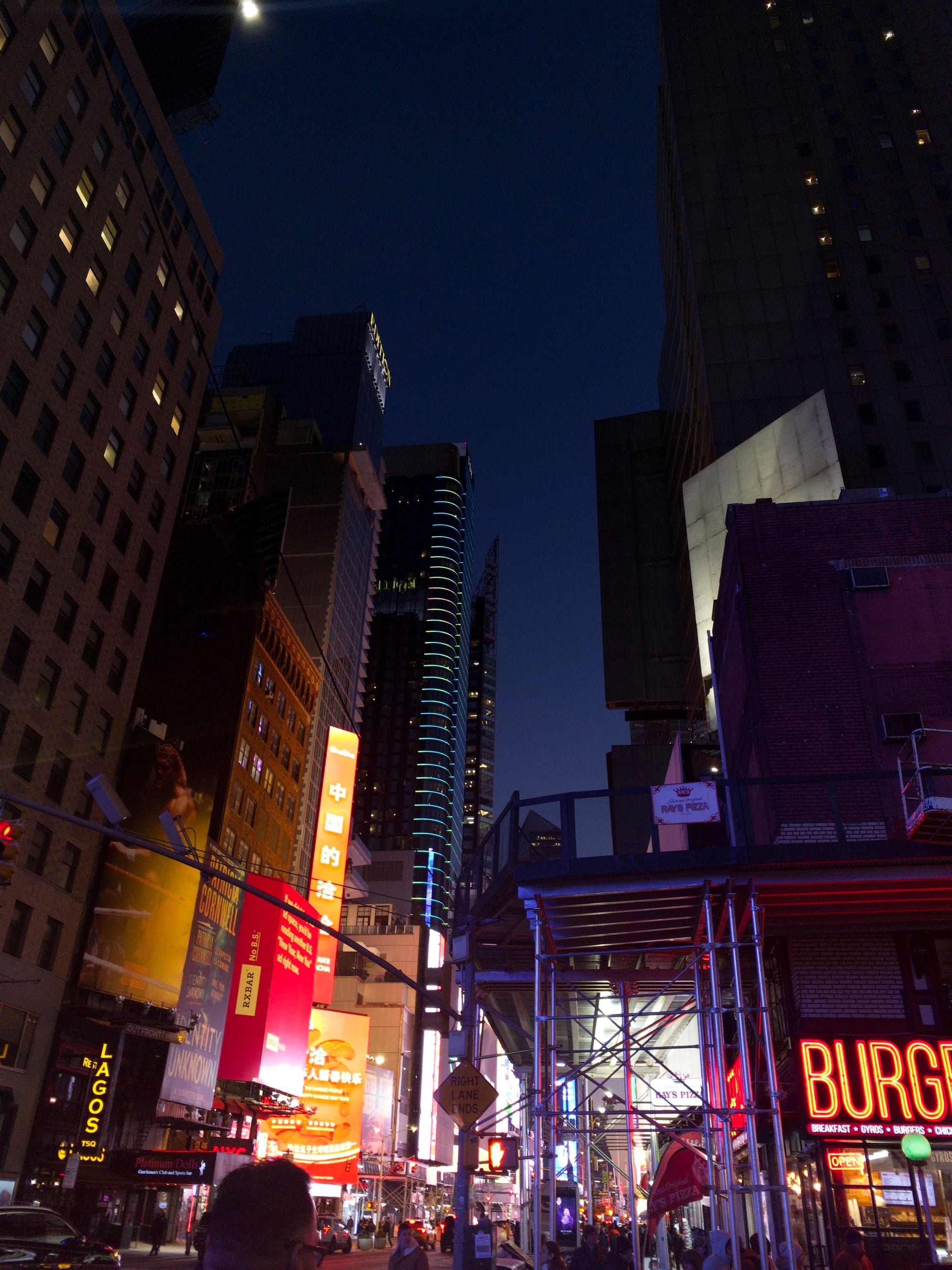 A bustling city street at night with illuminated signs and tall buildings, featuring a prominent Burgers sign