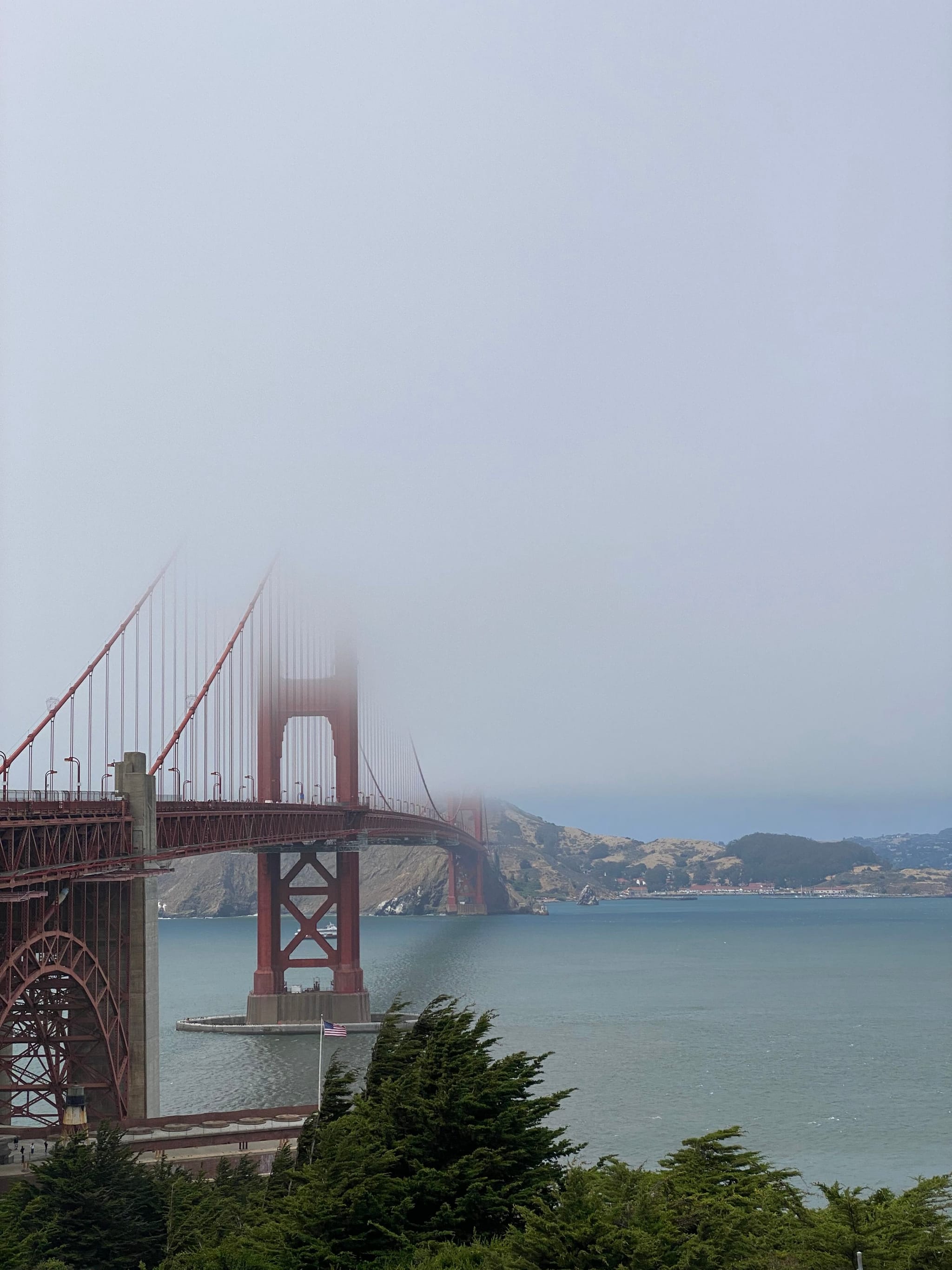 The Golden Gate Bridge partially shrouded in fog, with water and distant hills in the background