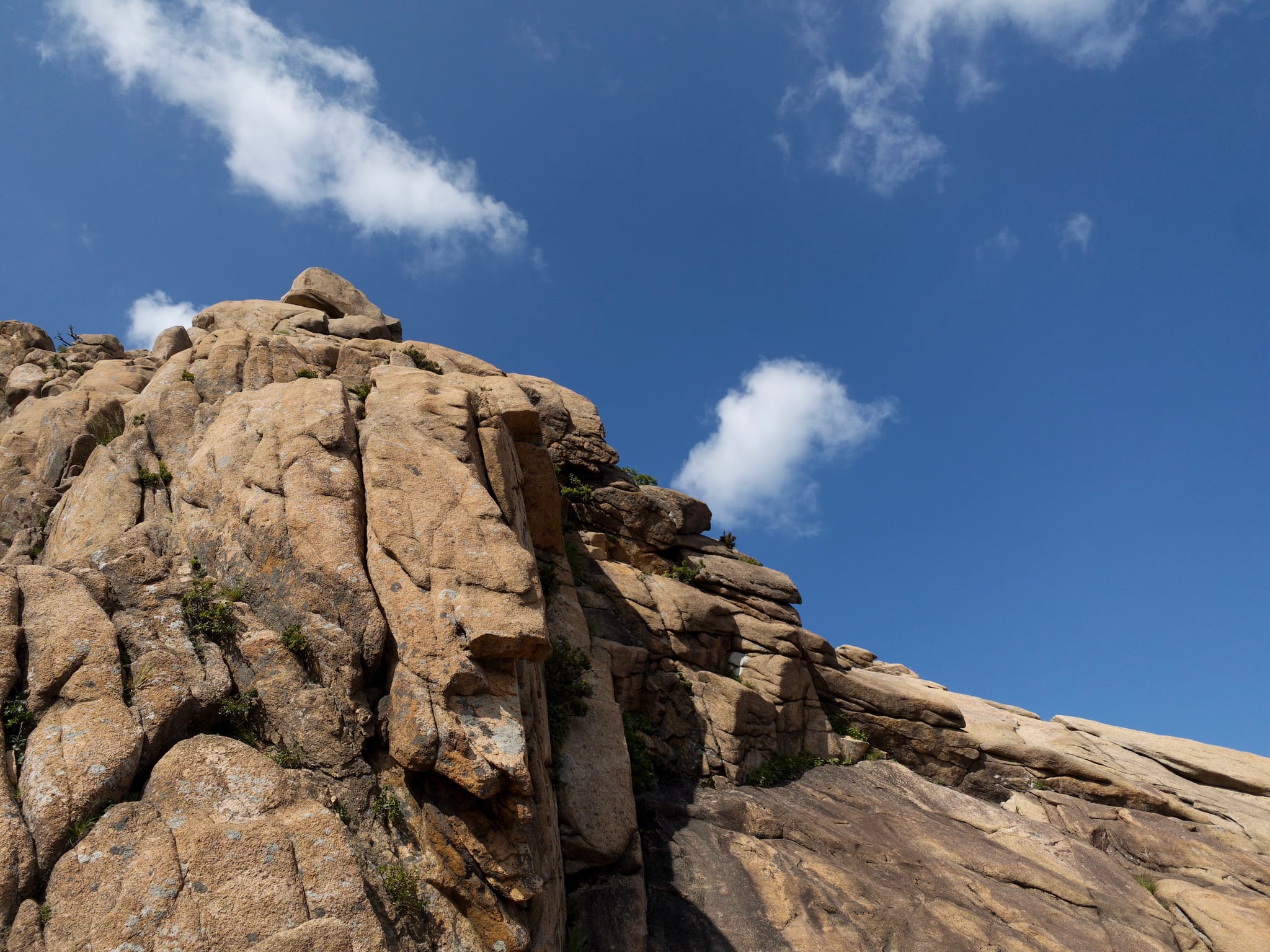 Rocky cliffs with some vegetation under a clear blue sky with a few clouds