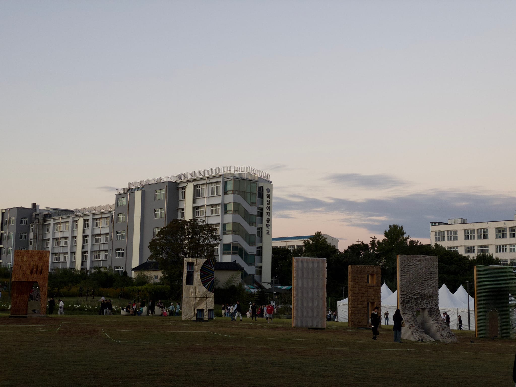 Sculptures on grassy area with modern buildings and people observing