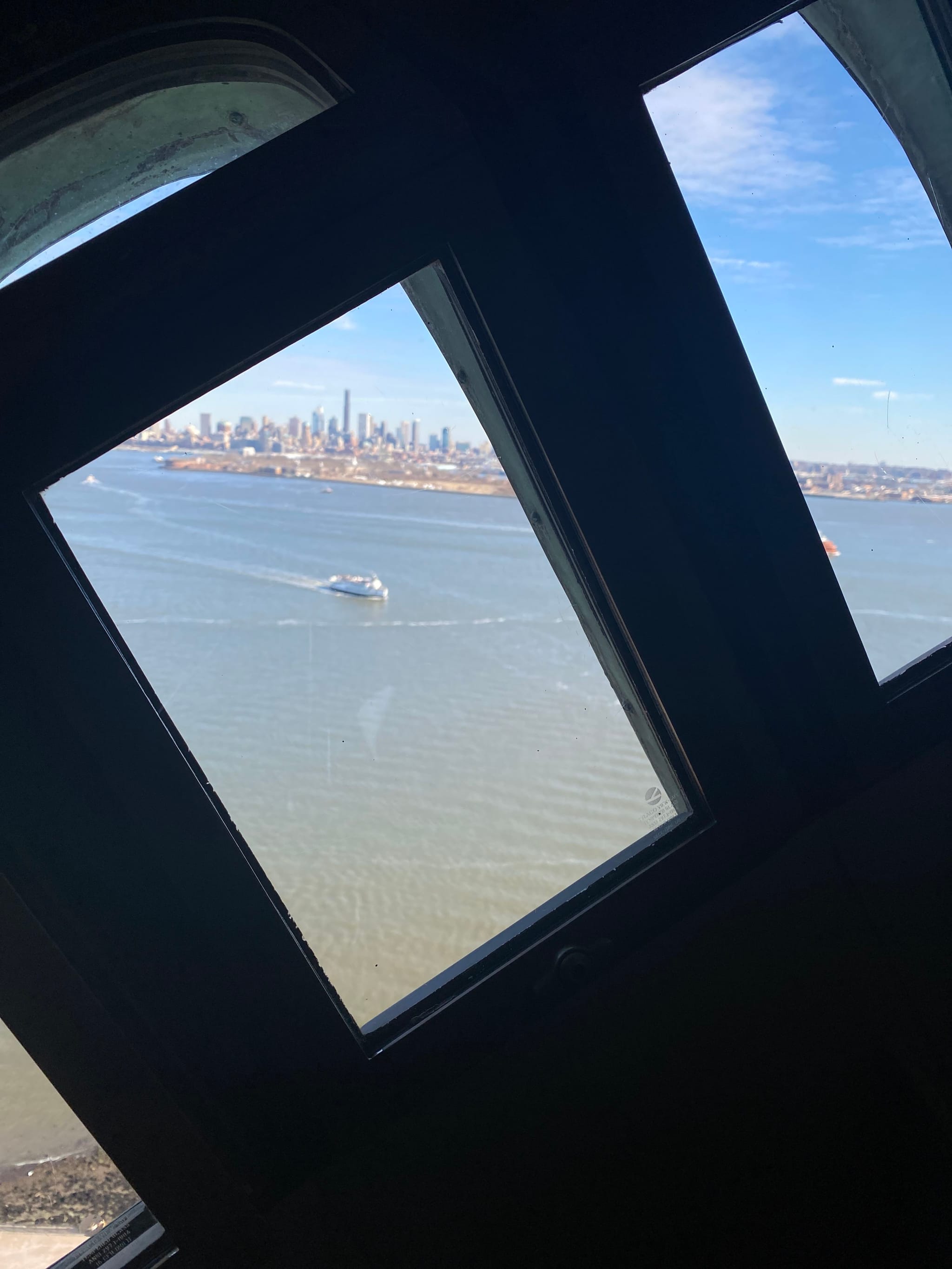 A view through a tilted window showing a body of water with a boat and a distant city skyline under a blue sky