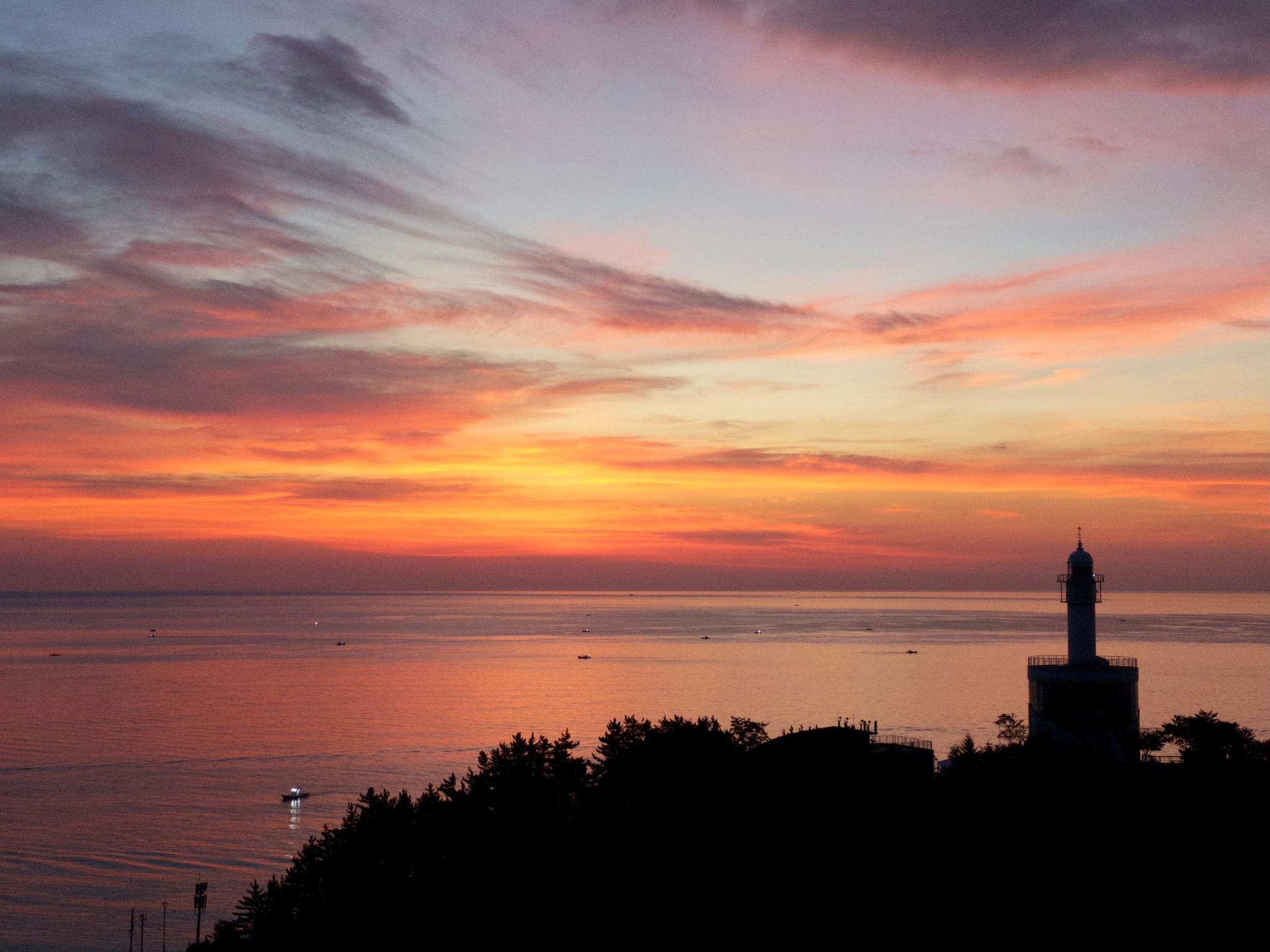 A sunset over the ocean with vibrant orange and pink hues in the sky, and a silhouetted lighthouse on the right