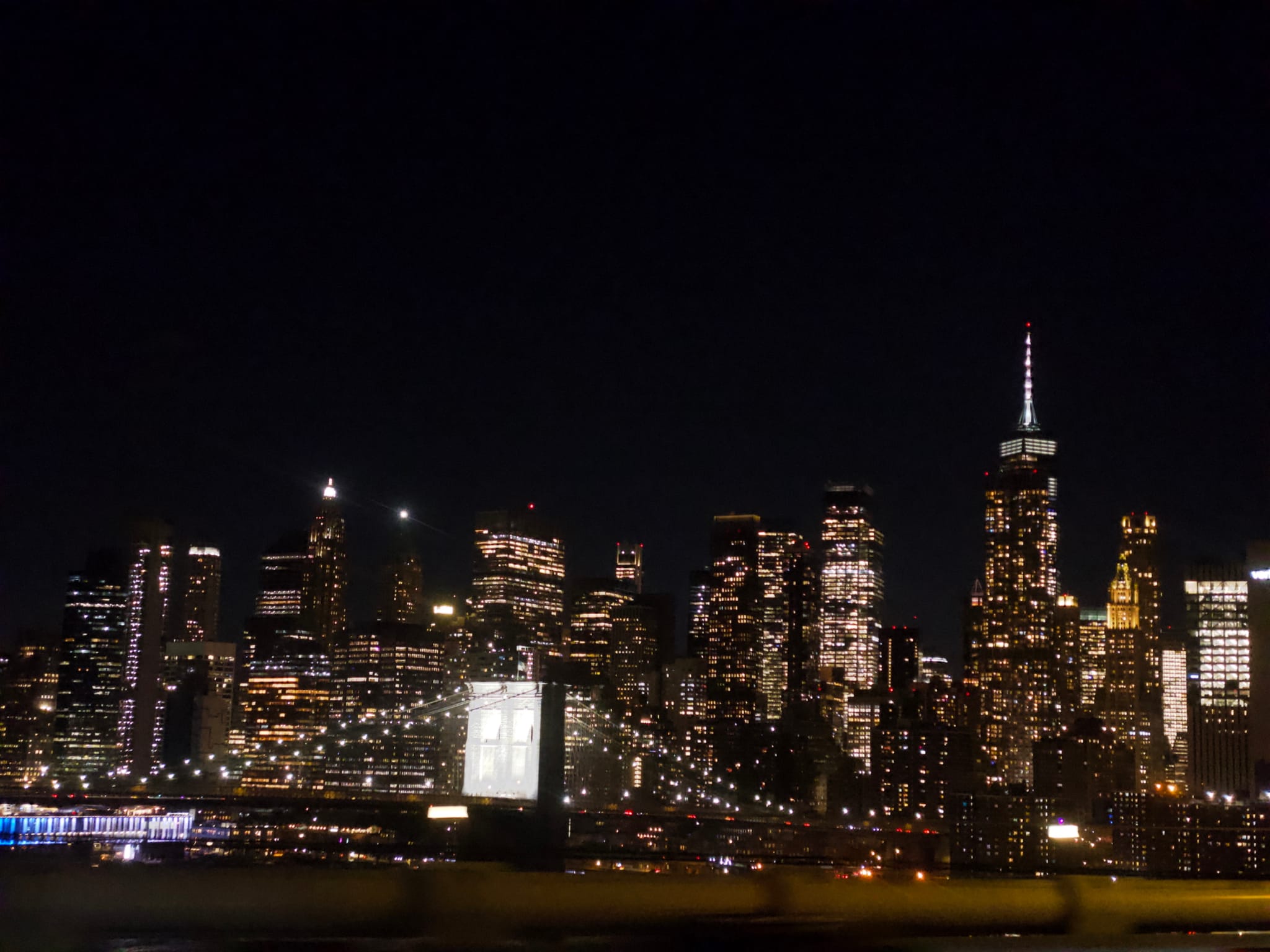 A city skyline at night with illuminated skyscrapers and a prominent bridge in the foreground