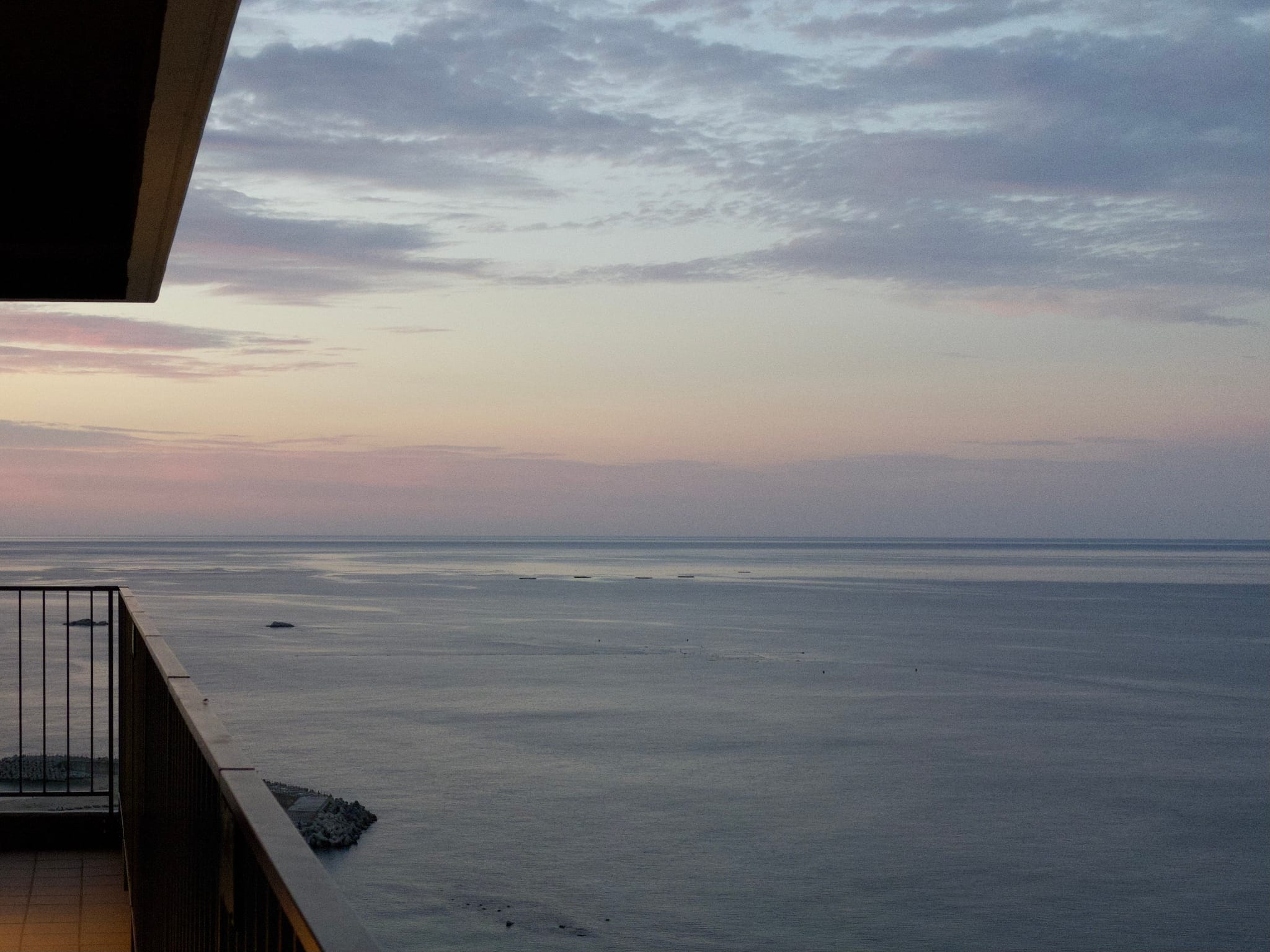 A calm ocean view at sunset with a balcony in the foreground, under a sky filled with soft, scattered clouds