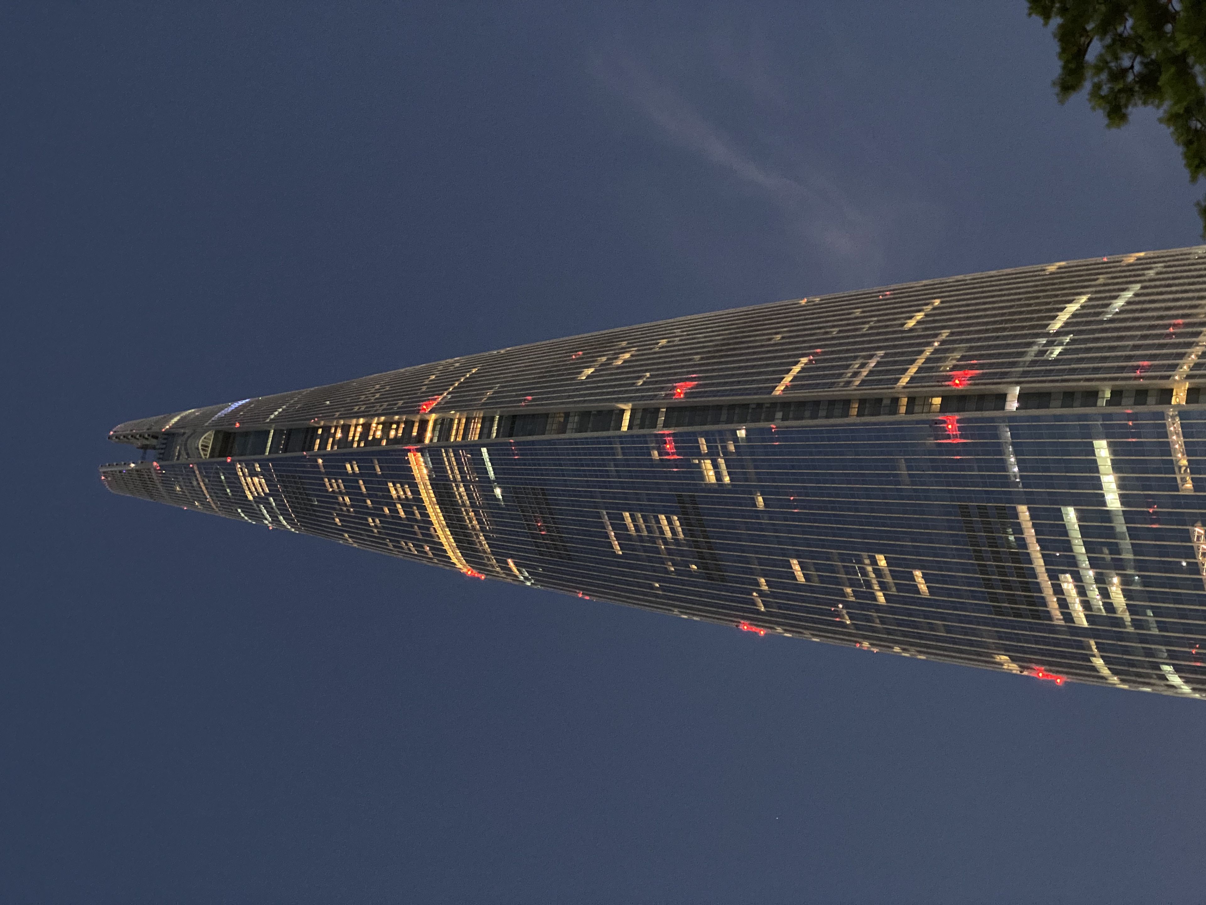 A tall, illuminated skyscraper with a sleek, tapering design against a dark evening sky