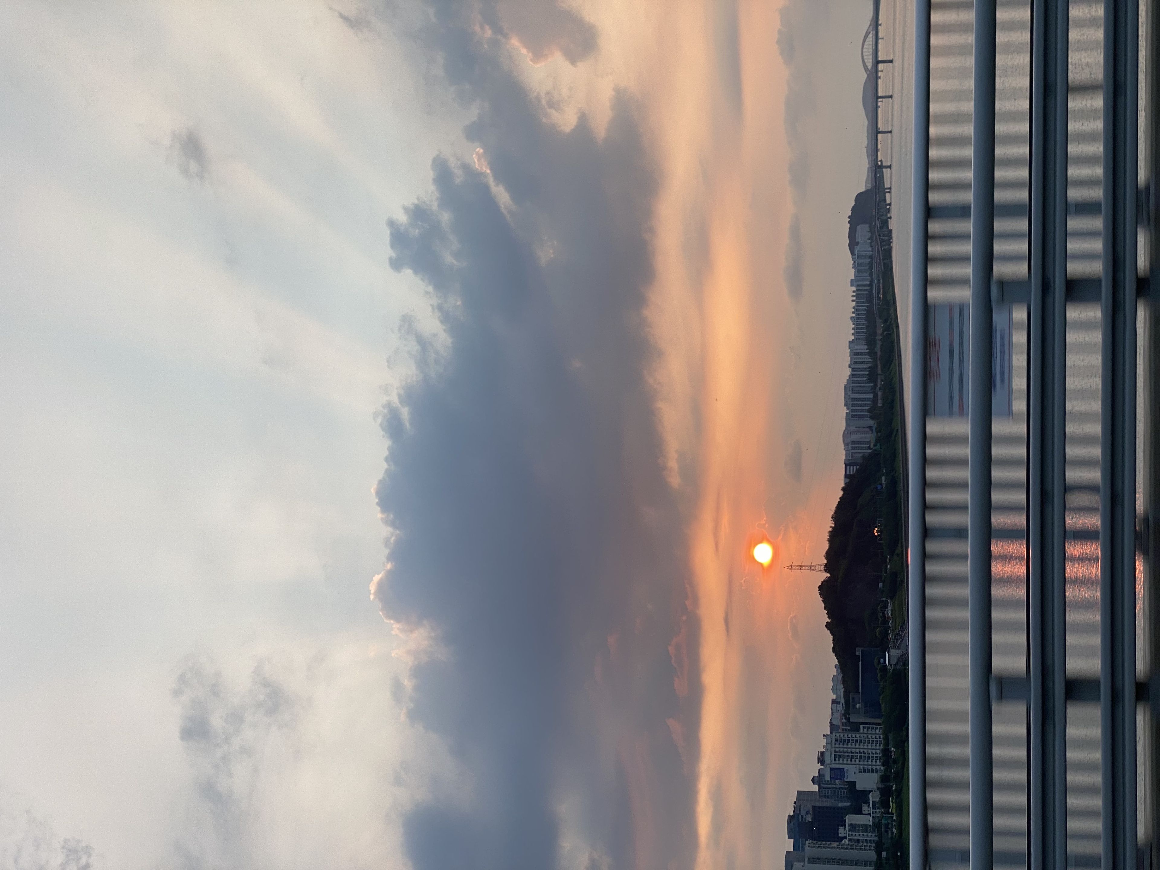A sunset over a cityscape with a river, bridge, and buildings silhouetted against a sky filled with clouds and sun rays