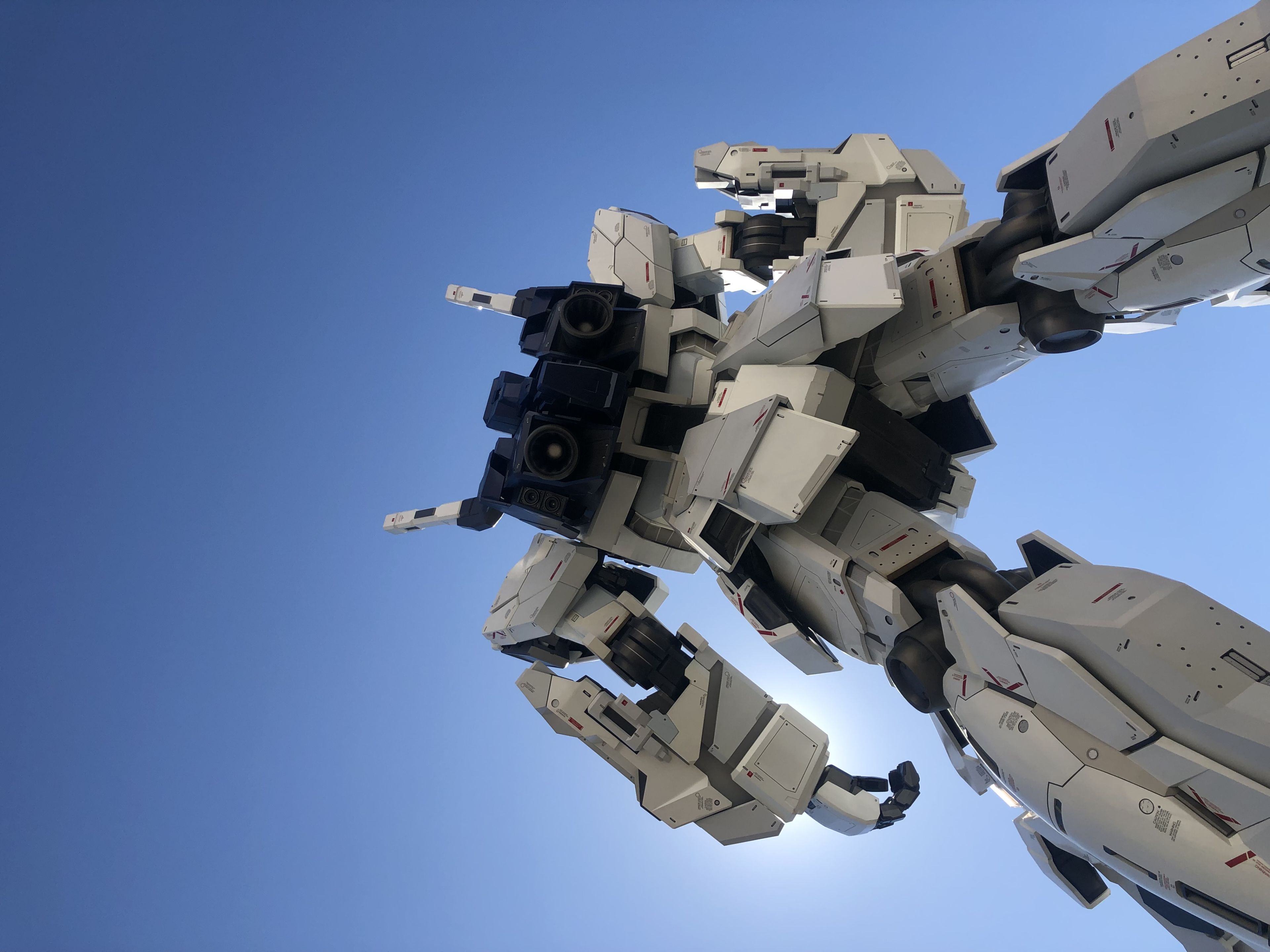 A large, white robot statue viewed from below against a clear blue sky