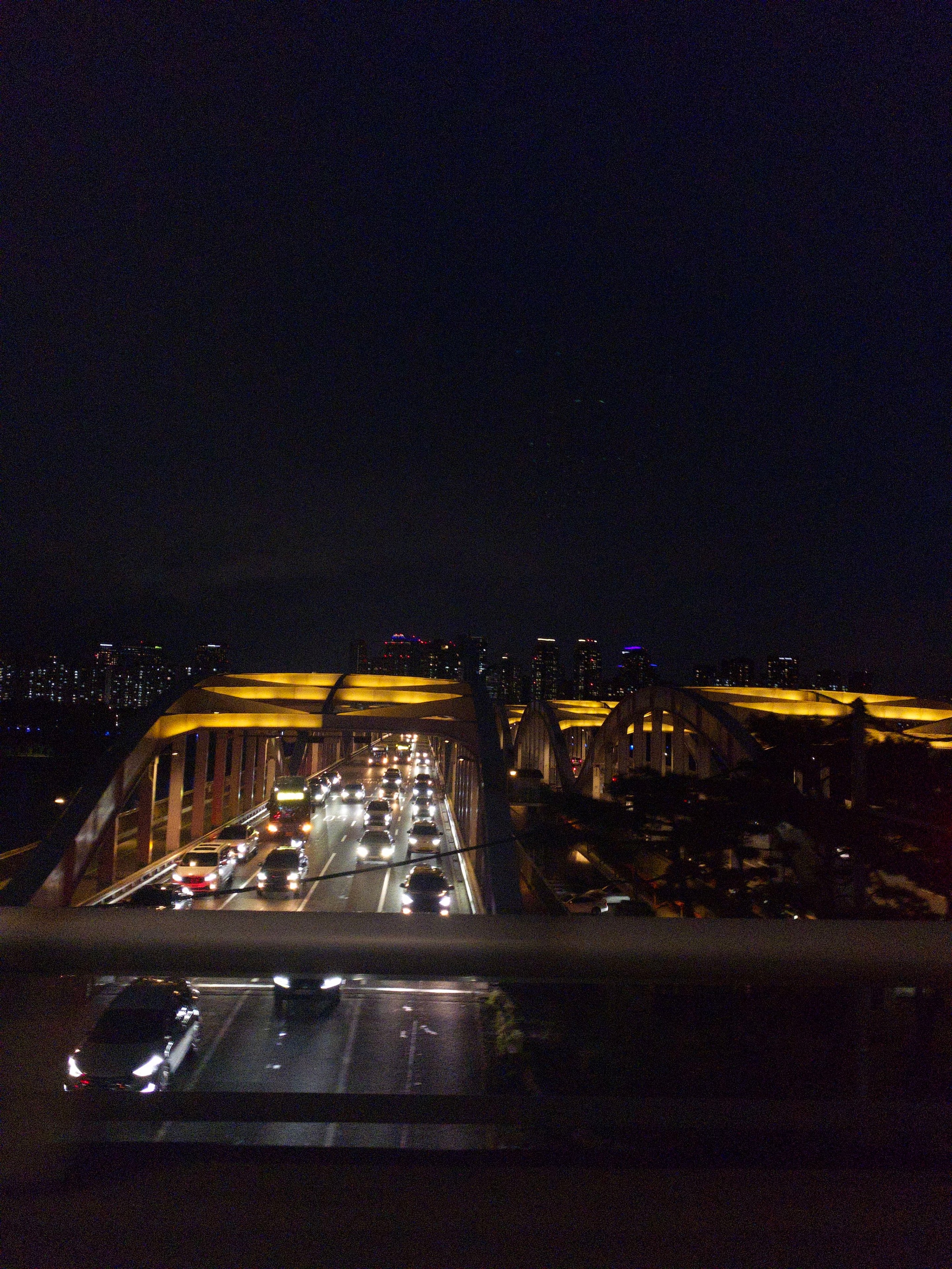 A nighttime view of a bridge with illuminated arches and vehicles traveling on it, set against a dark sky