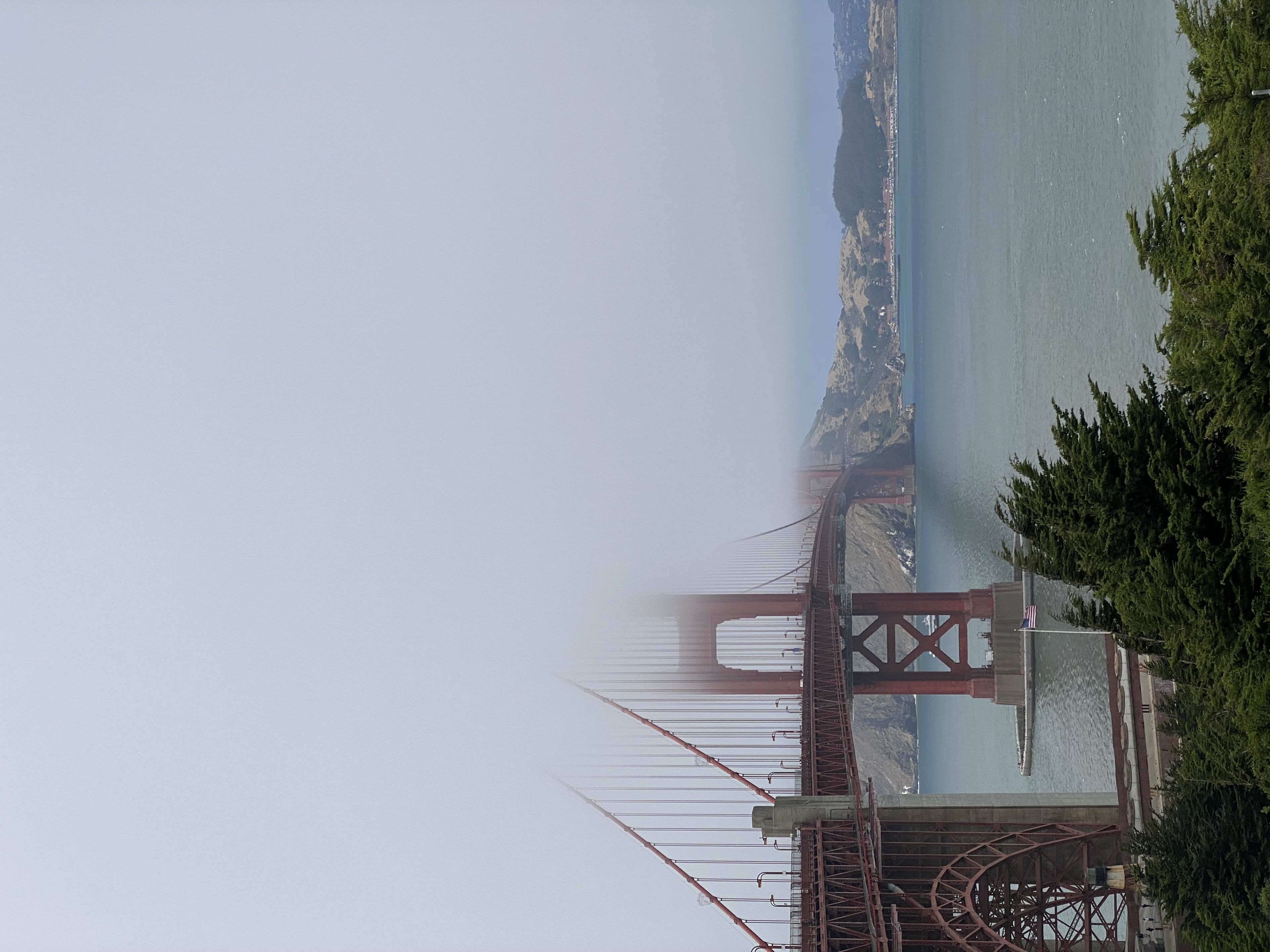 The Golden Gate Bridge partially shrouded in fog, with water and distant hills in the background