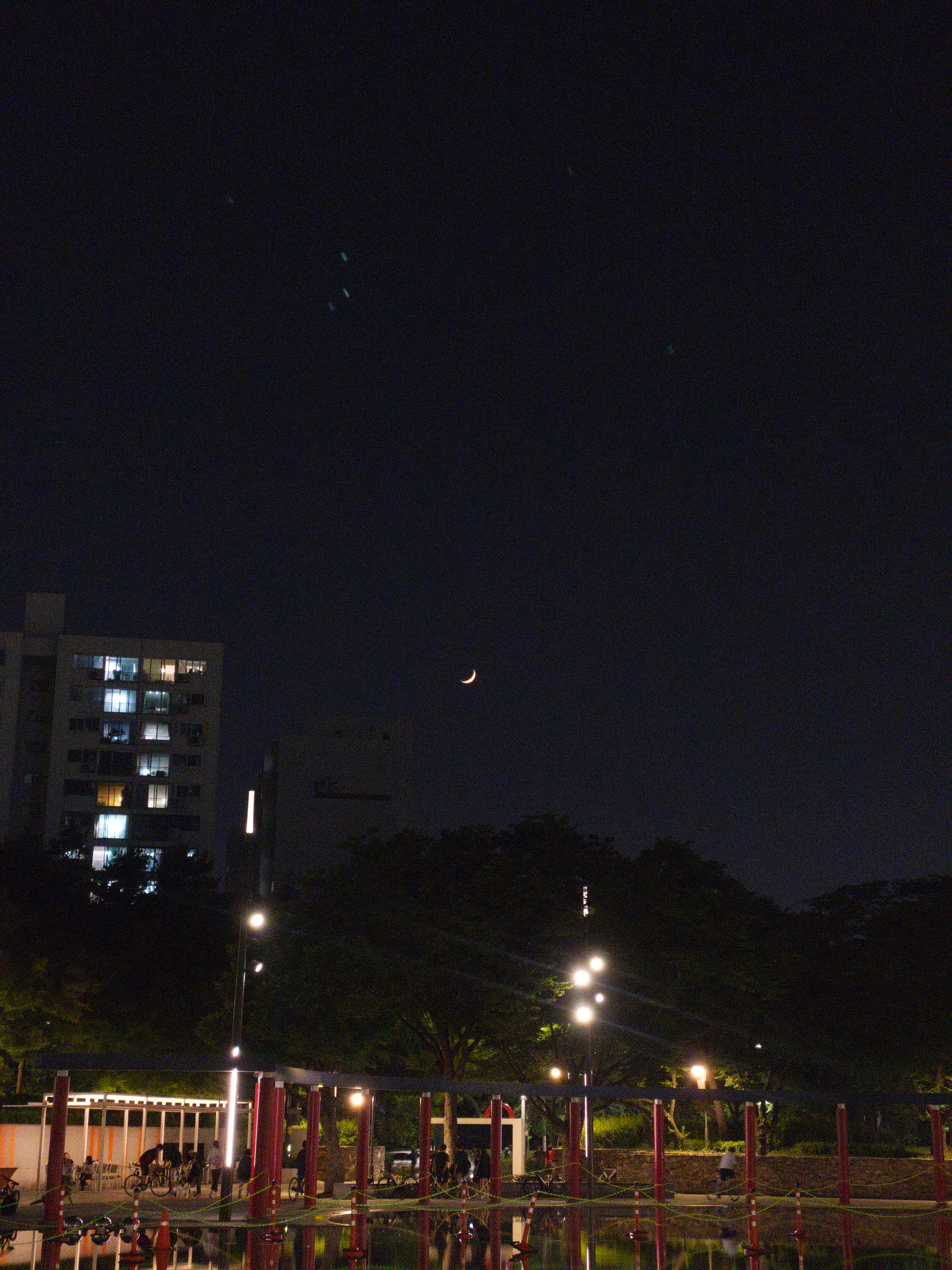 A nighttime scene with a crescent moon in the sky, city lights, and a building in the background